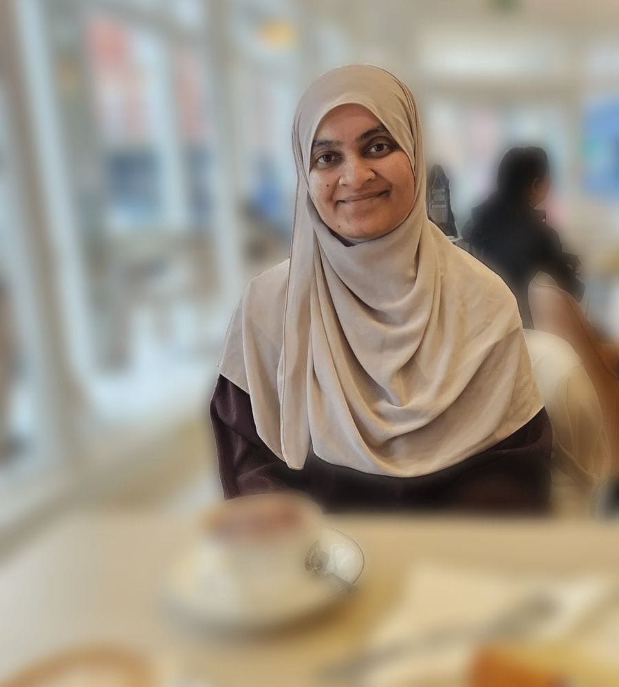 Smiling counsellor wearing a soft beige hijab, seated in a bright café
